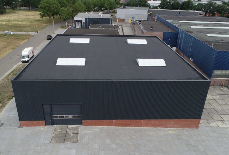 Nieuwe bedrijfshal - opslagruimte met zwarte beplating boven en rode stenen aan Laan van Indie Almelo